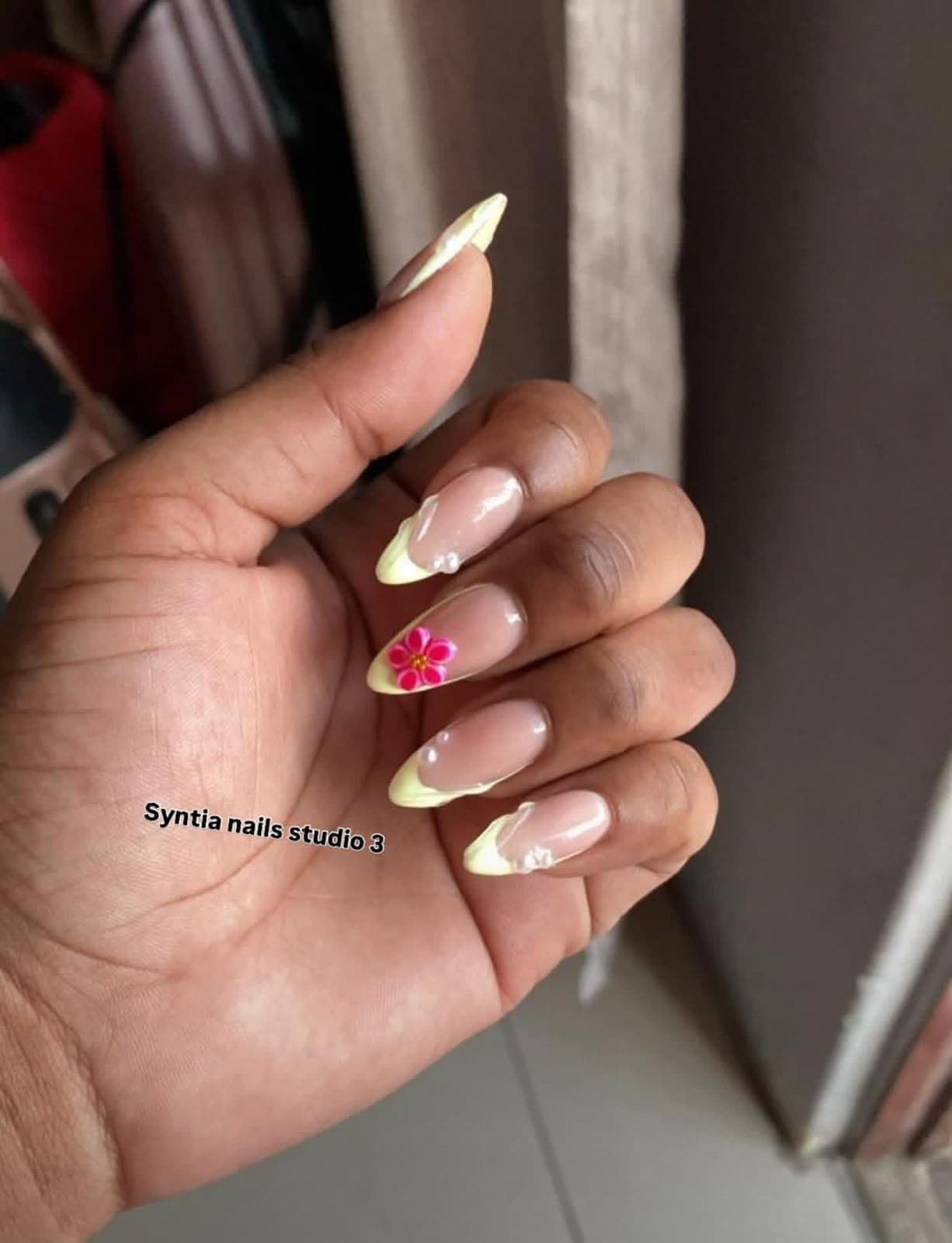 Almond nails with pastel yellow French tips, a 3D pink flower and pearl details