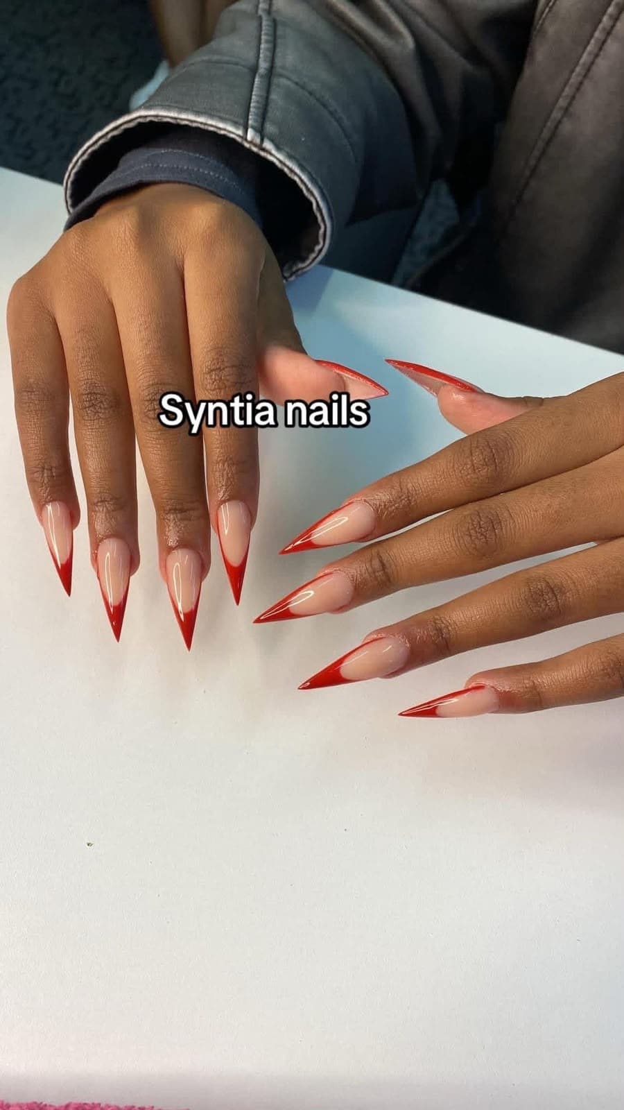 Long stiletto nails with nude base and glossy red French tips
